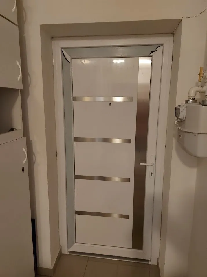 Utána: Régi, lakkozott fa ajtó helyett modern, fehér bejárati ajtó inox díszcsíkokkal.